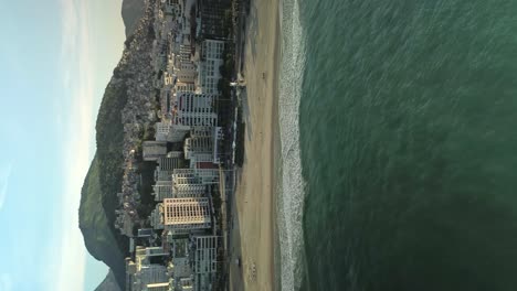 Sandy-beach-and-cityscape-of-Rio-de-Janeiro---aerial-pull-back,-vertical-video