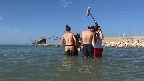 Film-troupe-immersed-in-sea-water-filming-scenes-of-boys-and-girls-playing-in-sea-in-summer-season-for-film-production