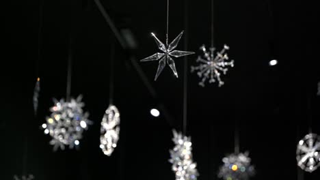 4k-white-sparkling-crystal-snowflakes-hanging-from-the-ceiling-shining-in-the-light-and-spinning-slowly-with-black-dark-background