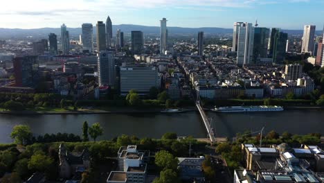 Panorama-Luftaufnahme-Der-Frankfurter-Innenstadt-Bei-Sonnenuntergang,-Während-Sich-Das-Licht-über-Lastkähne-Und-Fähren-Ausbreitet