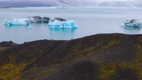 drone-aerial-view-of-the-magnificent-Jokulsarlon-lagoon-in-Iceland-with-its-icebergs-floating-on-the-surface-of-the-water-and-its-impressive-glacier-at-the-bottom,-cloudy-weather