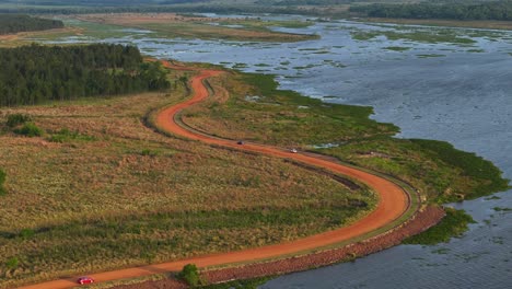 Cars-advancing-on-a-dirt-road-along-a-river-in-Misiones,-Argentina