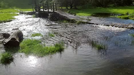 Overflowing-burst-riverbank-flooding-peaceful-sunlit-North-Wales-meadow-under-submerged-wooden-bridge-crossing