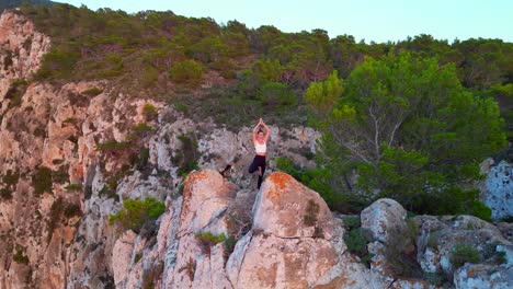 Atemberaubende-Luftaufnahme-Von-Oben-Flug-Ibiza-Klippe-Yoga-Baum-Pose-Modell-Mädchen-Sonnenuntergang-Abend