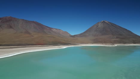 Aerial-drone-shot-flying-high-over-large-turquoise-colored-lake-water-surrounded-by-mountain-range-in-Bolivia-on-a-sunny-day