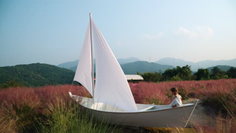 Hübsches-Mädchen,-Das-In-Einem-Hölzernen-Segelboot-Spielt-Und-So-Tut,-Als-Wäre-Es-Ein-Seemann-Auf-Dem-Rosafarbenen-Muhly-Grasfeld-–-Kräuterinselfarm-In-Pocheon-–-Ökotourismus-In-Südkorea