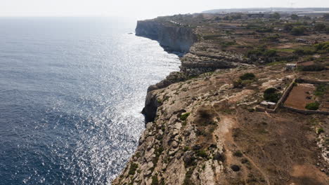 Aerial-view-following-the-steep,-rocky-shoreline-of-sunny-Malta-island