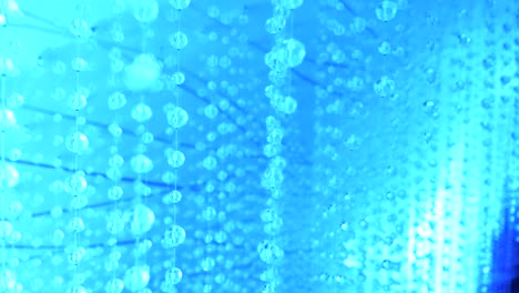 Lots-of-blue-crystal-orb-balls-hanging-on-threads-from-ceiling-immersed-in-blue-light