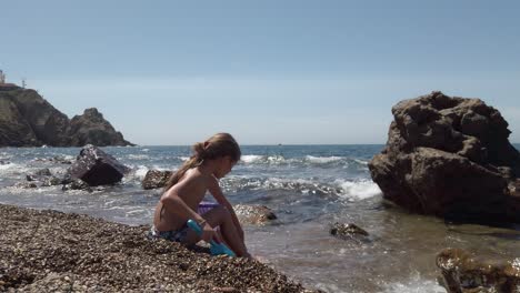 Langhaariges-Mädchen-Spielt-Mit-Kieselsteinen-Am-Strand-In-Spanien