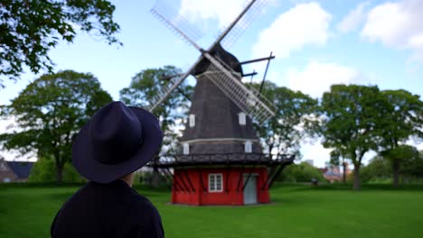 Man-wearing-a-hat-looking-at-a-traditional-Danish-windmill-in-Kastellet