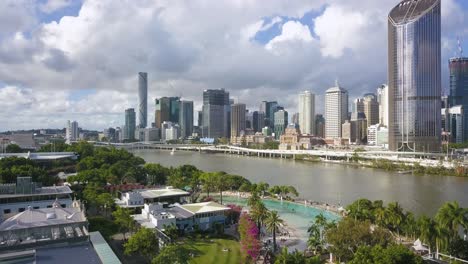 Drone-descends-below-palm-trees-hiding-view-of-Brisbane-Australia-skyline-and-river