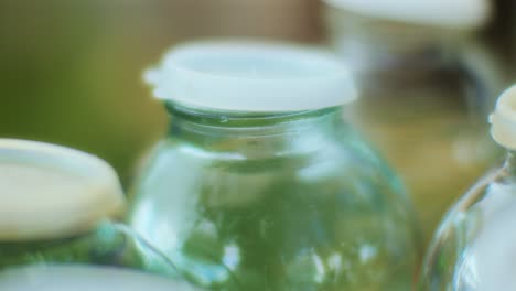 Close-Up-of-Empty-Glass-Bottles-with-Plastic-Lids-and-Tree-Reflections