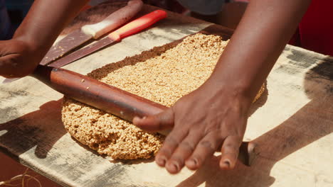 Close-up-of-hands-rolling-a-thick,-granular-dough-like-mixture-on-a-wooden-board