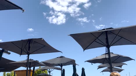 Beach-umbrellas-frantically-swaying-in-the-strong-wind-on-a-very-sunny-day-with-blue-sky-in-backgound
