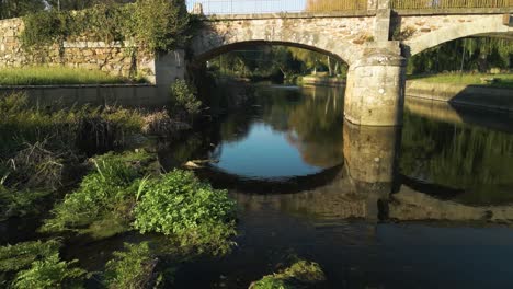 Flying-Under-The-Old-Stone-Bridge-Spanning-The-Anllons-River-In-Ponteceso,-A-Coruña,-Spain