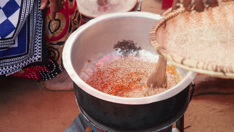 Traditional-African-cooking-scene-showing-hands-pouring-sesame-into-a-pot