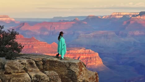 Woman-Standing-On-Edge-Of-The-Cliff-Looking-At-The-Scenic-Landscape-Of-Grand-Canyon-National-Park-In-Arizona,-USA---drone-shot