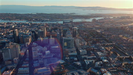 Downtown-Oakland,-California-business-district-and-harbor-at-sunset---aerial-flyover