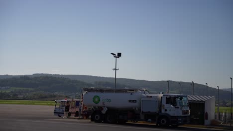 Small-propeller-airplane-taking-off-from-local-airport-with-BP-fuel-truck-in-front,-Pan-left-shot