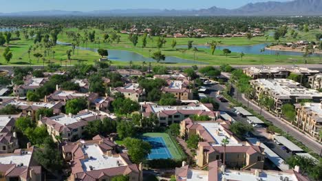 Southwest-USA-aerial-view:-lush-golf-courses,-water-features,-and-terracotta-roofed-residences,-with-mountain-backdrop-and-clear-blue-skies