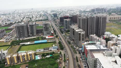 Aerial-drone-camera-passing-through-the-center-of-Rajkot-city-from-a-very-high-height-with-high-rise-buildings-in-front-and-low-rise-buildings-in-the-background
