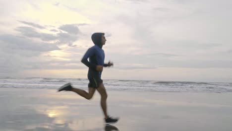 cinematic-low-down-video-of-a-fit-and-healthy-man-running-fast-down-the-wet-and-cold-beach-in-cornwall-in-england-just-before-the-sun-has-fully-risen-in-the-morning