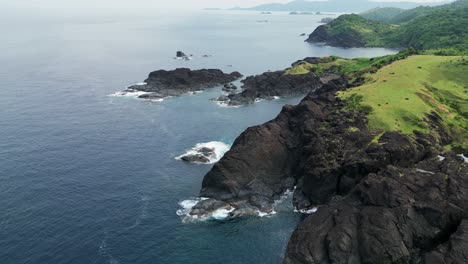Aerial-view-of-stunning-coastal,-island-rocks-and-lush-hills-facing-turquoise-ocean-waters