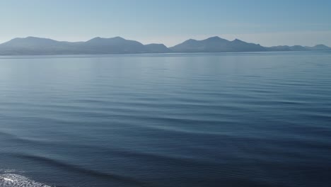 Dreamlike-misty-Snowdonia-mountain-range-vista-over-calm-tranquil-shimmering-blue-ocean-tide