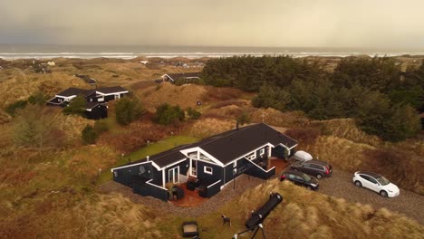 Modern-black-and-white-summer-house-in-the-countryside-by-the-ocean,-aerial-orbit