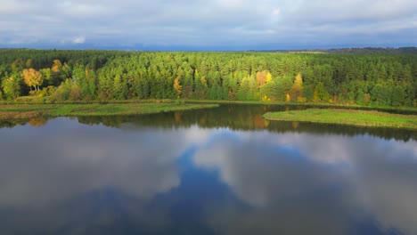 Mirrored-landscape-descending-drone-with-lake,-clouds,-autumn-forest-with-green-and-yellow-trees