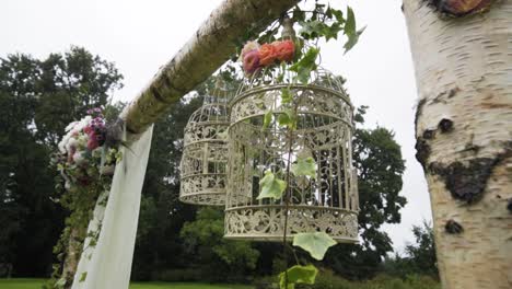 Zoom-in-on-wedding-birch-arch-white-empty-bird-cage-during-rainy-weather