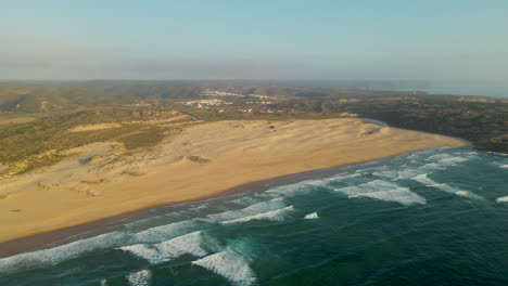Luftaufnahme-Des-Strandes-Von-Bordeira-Mit-Dünen-Und-Wellen,-Die-Während-Der-Goldenen-Stunde-Am-Ufer-An-Der-Westküste-Portugals-Brechen