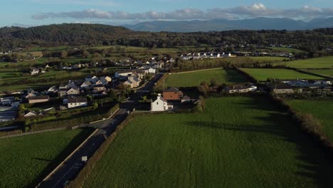 Descending-aerial-view-overlooking-rural-Welsh-village-surrounded-by-agricultural-farmland-countryside