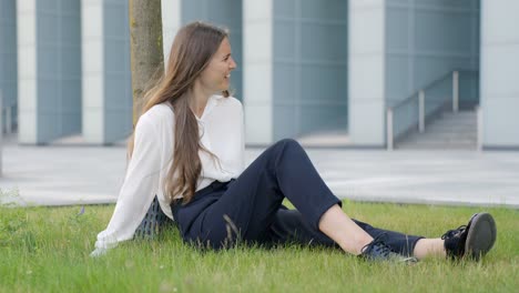 Girl-sitting-relaxed-on-grass-in-front-of-building-and-having-conversation