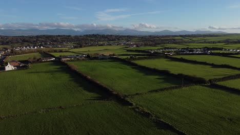 Aerial-view-flying-over-rich-vibrant-Welsh-green-agricultural-farmland-under-dramatic-glowing-sunset-sky