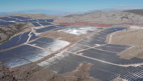 Drone-Sobre-Parque-De-Energía-Solar-Fotovoltaica-Paneles-De-Fila-Colinas-Rurales-Reflejo-De-La-Luz-Del-Sol