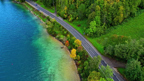 Aerial-view-of-a-black-car-traveling-on-an-asphalt-road-around-the-scenic-Attersee-Lake-in-the-Austrian-state-of-Upper-Austria,-Salzkammergut,-Europe