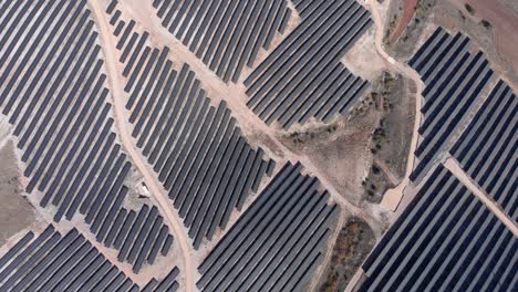 Top-down-drone-over-photovoltaic-solar-power-park-row-panels-hills-sunny-day