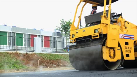 Workers-compact-the-asphalt-using-a-rolling-machine,-tandem-roller,-which-is-a-type-of-heavy-compactor-construction-vehicle-used-to-level-soil,-gravel,-concrete-or-asphalt-in-road-construction