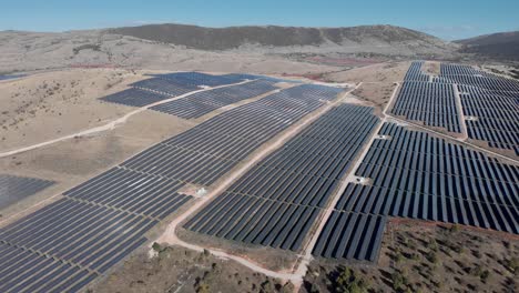 Descending-Drone-over-photovoltaic-solar-power-park-row-panels-hills-panning