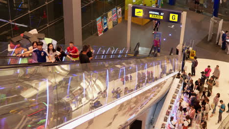 Shoppers-and-tourists-going-up-the-escalator-and-moving-around-the-shopping-mall-lobby,-in-a-business-district-in-Pattaya,-Thailand