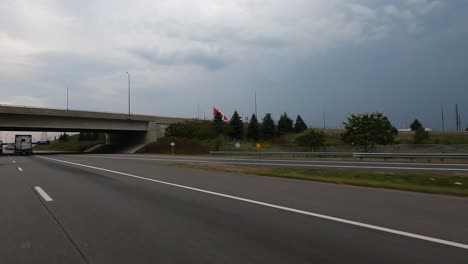 car-POV:-Canadian-road-with-flagpole-flying-national-flag-roadside