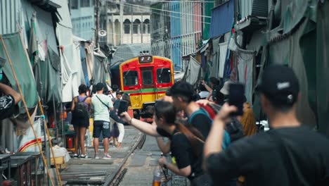 Train-travelling-in-Maeklong-Railway-Market-with-tourists-on-phones