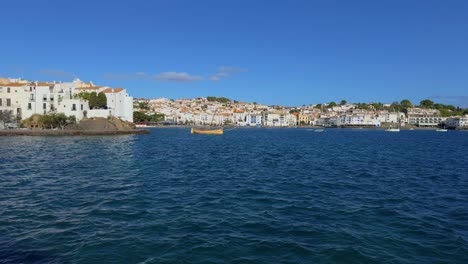 Cadaques-Mittelmeerstadt-An-Der-Costa-Brava-Von-Girona,-Blick-Auf-Das-Tiefblaue-Meer-Und-Die-Reihe-Weißer-Häuser-Und-Ein-Gelbes-Boot-Im-Wasser