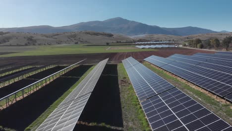 Drohne-über-Photovoltaik-Solarpanel-Parkbauernhof,-Blauer-Himmel,-Felder,-Berghintergrund
