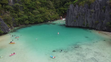 Aerial-overview-of-kayak-and-paddlers-exploring-clear-blue-water-of-cadlao-lagoon
