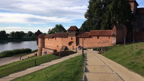 Nogat-river-waterfront-in-Malbork,-Poland-at-beautiful-sunset-with-a-castle,-the-red-brick-walls-and-tourists