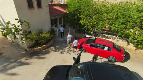 Aerial-tracking-shot-of-men-leaving-car-and-entering-home-on-sunny-day