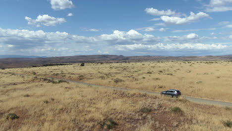 Drone-shot-tracking-a-modern-SUV-driving-in-a-prairie-scenery,-sunny-day-in-USA