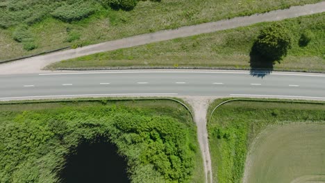 Aerial-establishing-shot-of-a-rural-landscape,-countryside-road-with-trucks-and-cars-moving,-lush-green-agricultural-crop-fields,-sunny-summer-day,-wide-birdseye-drone-dolly-shot-moving-left